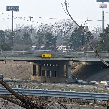 Guardrail and embankment in foreground, then freeway with view of bridge overpass.