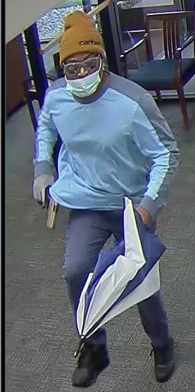 Thin black man in dark pants, light blue long sleeve shirt, brown Carhartt hat, with glasses.